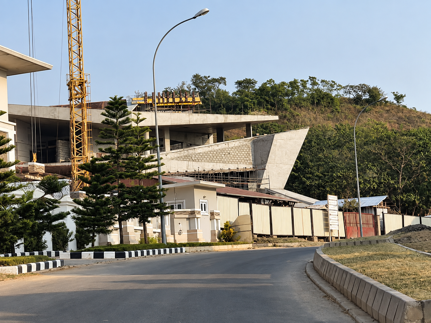 Street level view of Alexence Villa under construction, with the cantilevered concrete roof and angular volumes rising above the site fence