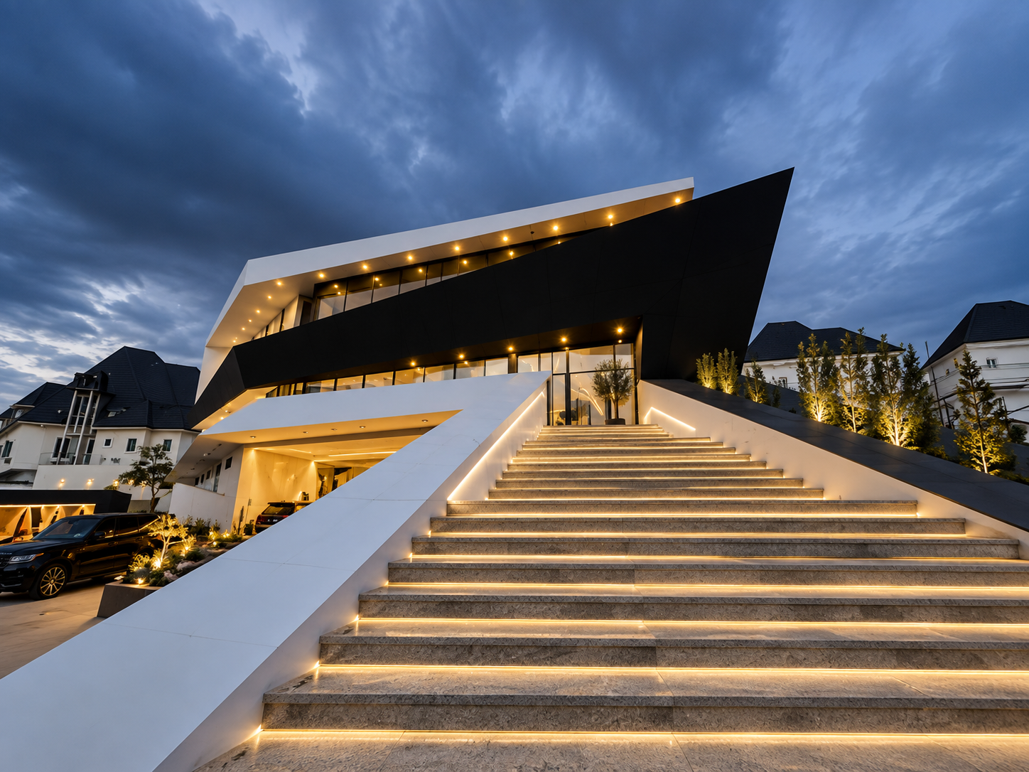 Alexence Villa completed at dusk in Abuja, with the grand illuminated stone stair, glowing interiors and the cantilevered dark roof plane against an evening sky