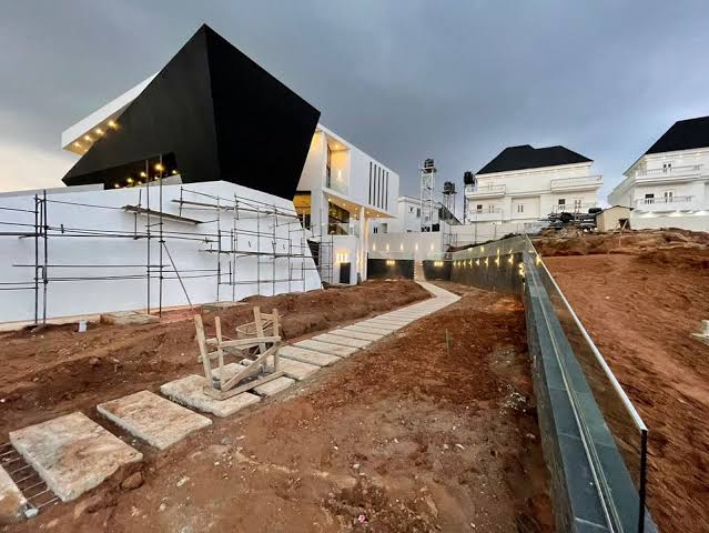 Alexence Villa under construction at dusk, with the black folded roof plane cantilevering over the terrace and the lit stone walkway across the site